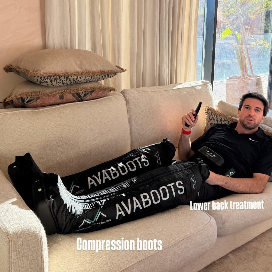 Racing driver Félix da Costa reclining on a sofa, wearing the AVABoots compression boots (labelled "Compression boots") and a lower back device (labelled "Lower back treatment"), during an at-home recovery session.