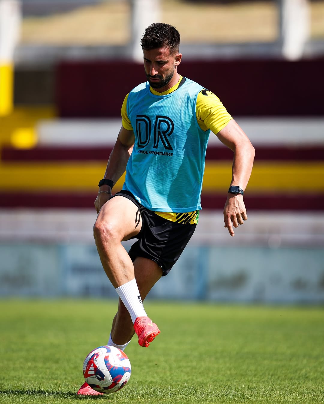 Football player training in a blue DR Futebol Performance bib, controlling a soccer ball on the pitch with focus and intensity.