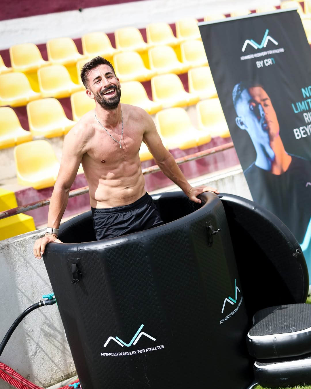 Atleta sorridente a fazer crioterapia num banho de gelo da AVA – Advanced Recovery for Athletes, durante uma sessão de recuperação num estádio.