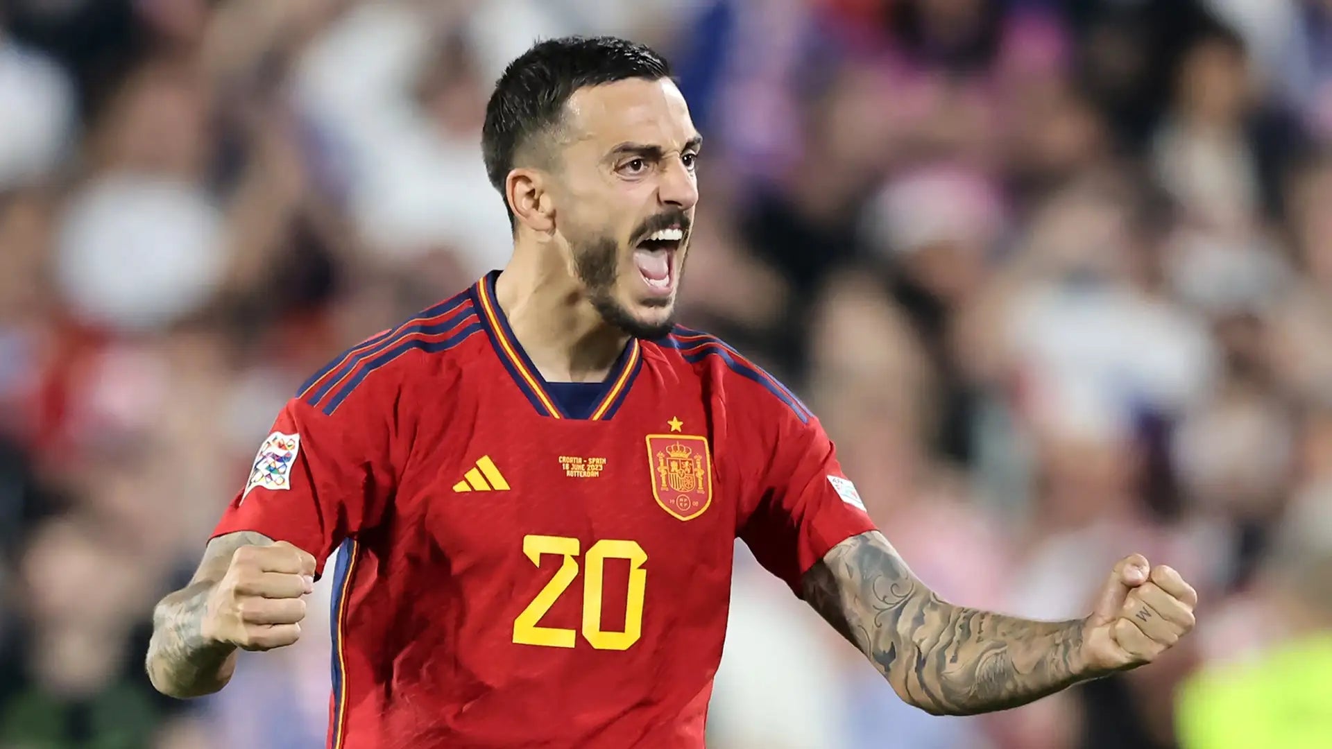 Jogador da selecção espanhola de futebol grita e celebra com os punhos cerrados, exibindo expressão de intensa emoção. Veste o equipamento vermelho oficial com o número 20 e o emblema da Federação Espanhola ao peito, durante um jogo da Liga das Nações da UEFA.