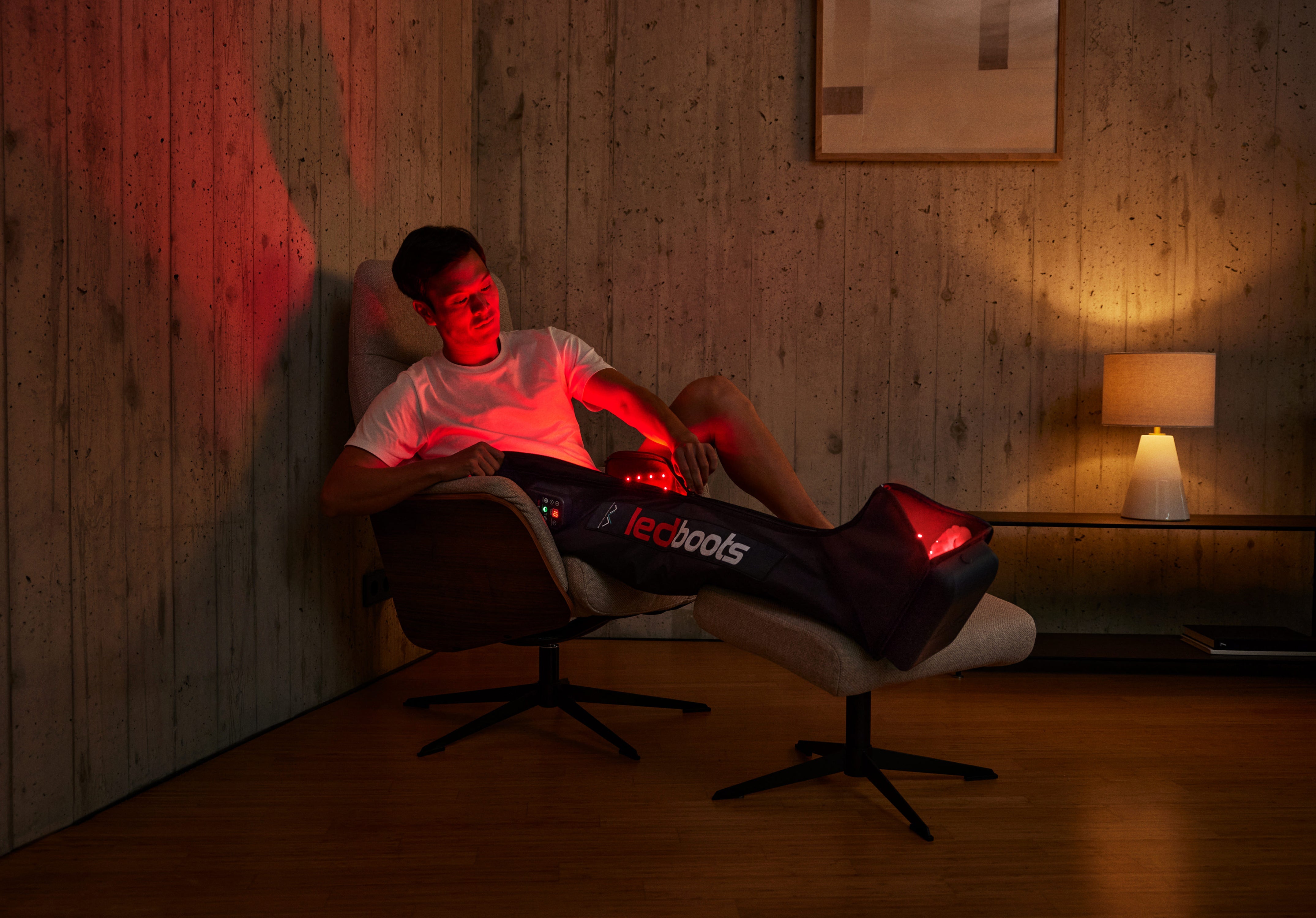 Man sitting in an armchair using the AVA by CR7 Led Boots, compression recovery boots with red LED light therapy designed to accelerate muscle recovery, reduce fatigue, and improve blood circulation at home